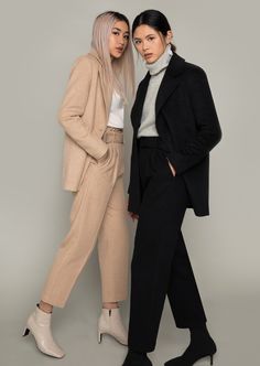 two women standing next to each other in front of a gray background wearing black and white outfits