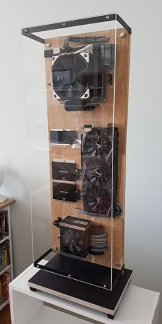 a display case with various electronics in it on top of a white table next to a bookshelf