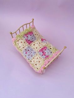 a crocheted baby's bed is shown on a purple background with gold pins