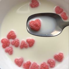 a spoon filled with milk and some red hearts on it's side in a bowl