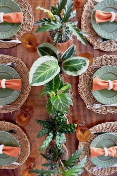 an overhead view of a table with place settings and green plates, orange napkins and greenery