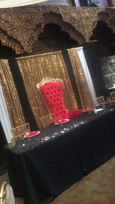 a red chair sitting on top of a black table covered in gold sequins