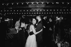 black and white photo of bride and groom dancing at their wedding reception with guests in the background