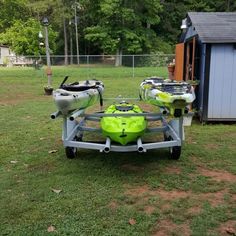 two kayaks are sitting on a trailer in the grass next to a shed and fence