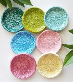 six colorful plates sitting on top of a white table next to green leafy plants