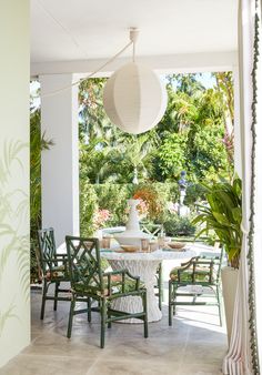 an outdoor dining area with green chairs and a white table surrounded by greenery in the background