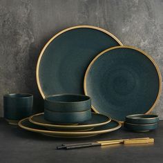 a set of green and gold dinnerware on a table with a pen next to it