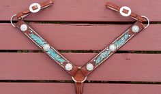 a brown and blue tooled horse bridle on a pink wooden bench with white flowers