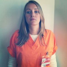 a woman in an orange prison uniform is standing against a wall and looking at the camera