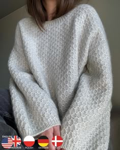 a woman wearing a white sweater and jeans sitting on top of a couch with her hands in her pockets