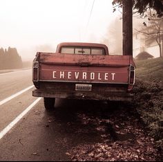 an old chevrolet truck is parked on the side of the road in front of a tree