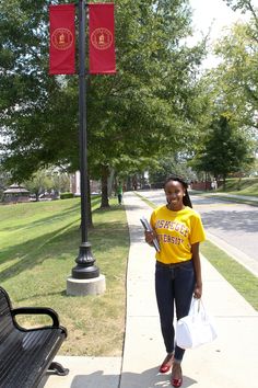 a woman in a yellow shirt is walking down the sidewalk with shopping bags and a cell phone