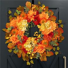 an orange and yellow wreath is hanging on a black door with autumn leaves around it