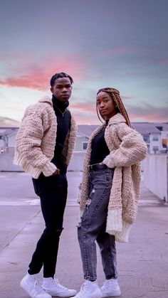 two people standing next to each other in front of a building with the sun setting behind them