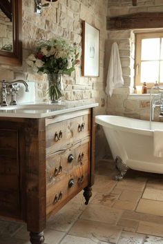 a white bath tub sitting under a window next to a sink and a wooden cabinet