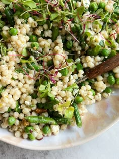 a white plate topped with green vegetables and grains next to a wooden spoon on top of a table