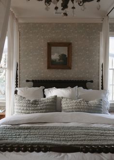 a bed with white linens and pillows in a bedroom next to a painting on the wall