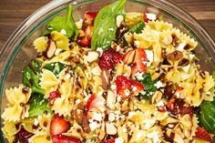 a salad with strawberries, spinach and nuts in a glass bowl on a wooden table