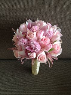 a bouquet of pink roses and carnations sits on a couch next to a pillow