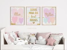 two pink and gold prints on the wall above a white day bed with stuffed animals