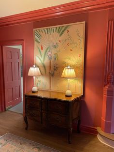 a room with red walls and two lamps on top of the dresser in front of it