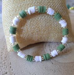 a green and white beaded bracelet sitting on top of a pillow