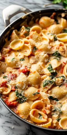 a skillet filled with pasta and spinach on top of a marble countertop