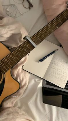 an open notebook and pen sit on top of a guitar