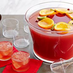 two glasses filled with red liquid and orange slices on top of each glass next to other glasses