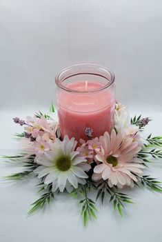 a pink candle surrounded by flowers and greenery