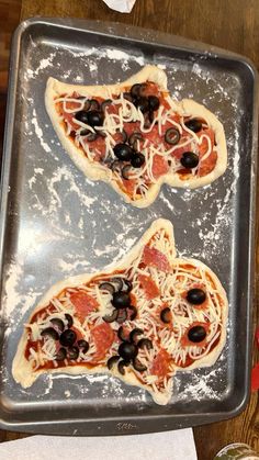 two uncooked pizzas sitting on top of a metal pan covered in cheese and olives