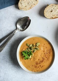 a white bowl filled with soup next to two slices of bread and a spoon on the side