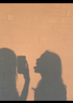 the shadow of a person holding a cell phone in front of a wall with a brick background