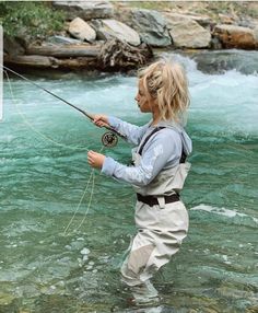 a woman standing in the water while holding a fishing rod