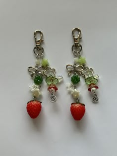 two strawberry charms are attached to each other on a white surface with green and red beads