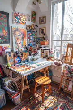 an artist's studio with lots of art supplies on the table and in front of large windows