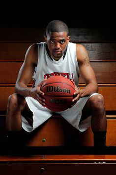 a man sitting on a bench with a basketball in his hand and wearing a jersey