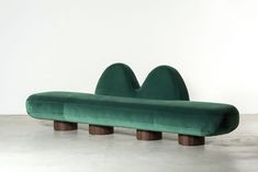 a large green couch sitting on top of a cement floor next to a white wall