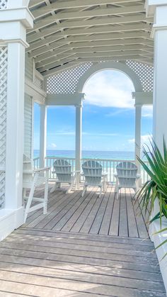 two lawn chairs sitting on top of a wooden deck next to the ocean with an arch