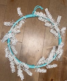 a wreath made out of white flowers and blue string on a wooden floor with wood floors