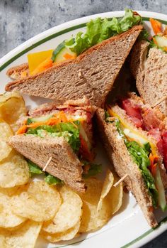 a sandwich with lettuce, tomato, cheese and chips on a plate next to some potato chips