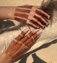 two hands are painted with red and white stripes on the skin of a horse's head