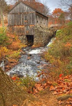 an old wooden bridge over a small stream in the woods with fall foliage around it