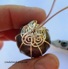 a person is holding a wire wrapped around a bead with an intricate design on it