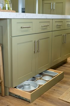 an open drawer in the middle of a kitchen with plates and bowls on it's bottom shelf