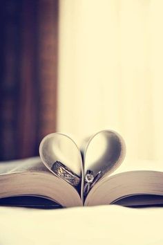 an open book with two heart shaped pages on top of it, sitting on a bed