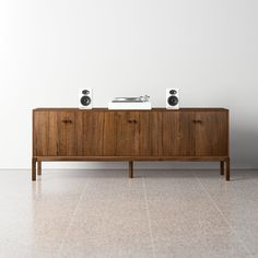 two speakers sitting on top of a wooden cabinet in an empty room with tile flooring