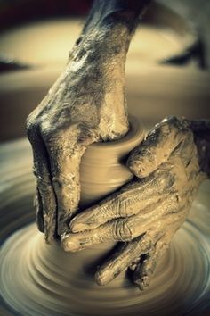 two hands on a potter's wheel with their fingers touching each other over the pottery