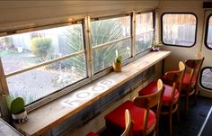 the inside of a bus with red seats and wooden tables in front of windows that read boooo