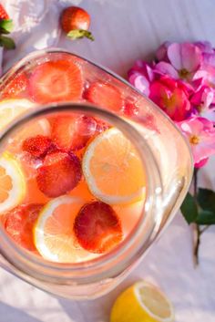 a pitcher filled with lemons and strawberries on top of a table next to flowers